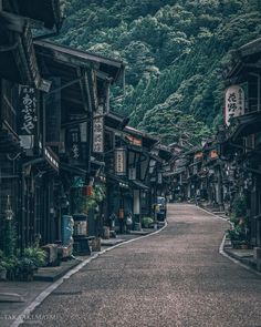 an empty street lined with wooden buildings in the middle of a forested area, surrounded by mountains