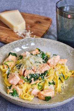 pasta with salmon, spinach and parmesan cheese in a bowl next to a glass of water