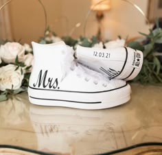 a pair of white shoes with the word mr and mrs painted on them sitting on a table next to flowers