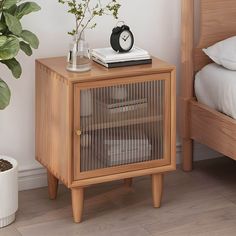 a small wooden cabinet sitting next to a bed with a plant on top of it