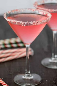 two pink cocktails with candy canes on the table next to eachother