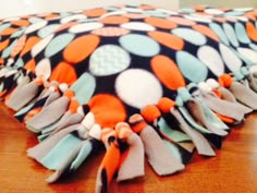 an orange and black polka dot blanket with tassels on the edge sitting on a wooden table