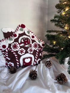 a house made out of crochet next to a christmas tree with pine cones