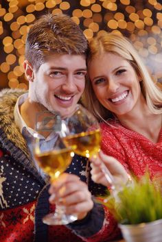 a young man and woman are holding wine glasses in front of the camera with christmas lights behind them