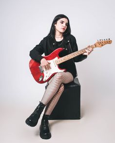 a woman sitting on top of a black stool holding a red and white electric guitar