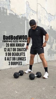 a man standing next to two black dumbbells in front of a concrete wall