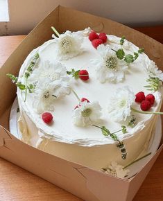 a cake in a box with white flowers and raspberries on the top is ready to be eaten