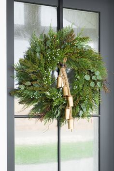 a christmas wreath hanging on the side of a window next to a door with bells