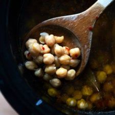 a wooden spoon filled with chickpeas in a crock pot on top of a table