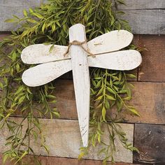 a white dragonfly hanging on a wooden wall with green leaves and twigs around it