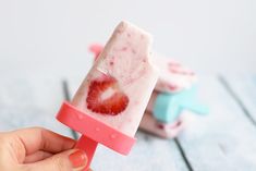 a hand holding an ice lolly popsicle with strawberries on it