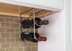 three bottles of wine are hanging on the wall in front of a tile backsplash