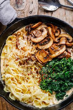 pasta with mushrooms, spinach and cheese in a skillet on a wooden table