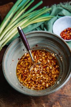 a bowl filled with food sitting on top of a wooden table next to green onions