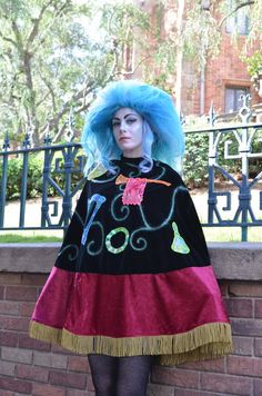 a woman with blue hair wearing a black and red dress standing next to a brick wall