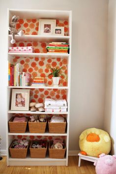 a white book shelf filled with books next to a pink stuffed animal and other toys