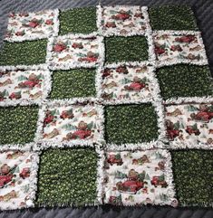 a quilted blanket with red trucks and green grass on it's sides, sitting on a bed