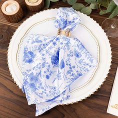 a blue and white plate with a napkin on it next to some wine glasses and candles