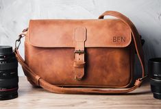 a brown leather bag sitting on top of a wooden table next to two black cameras