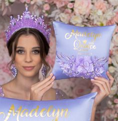 a woman is holding two pillows with the names of their princesses on them and there are flowers in the background