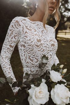 a woman wearing a white lace dress and holding a bouquet of flowers in her hand