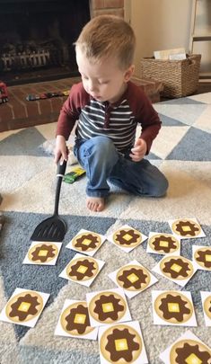 a little boy sitting on the floor playing with some cut out cookies and a spatula