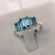 a three stone ring with blue topazte stones on it's sides, sitting on a white surface