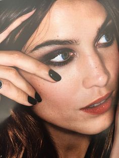 a woman with black nail polish holding her hand up to her face and looking at the camera