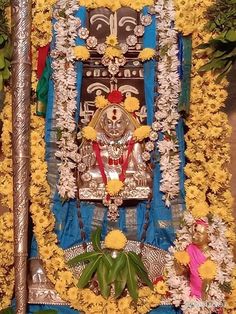 the idol is surrounded by yellow flowers and other decorations in front of a wall covered with greenery