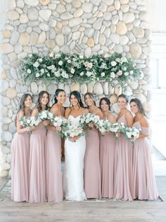 a group of women standing next to each other in front of a stone wall with flowers