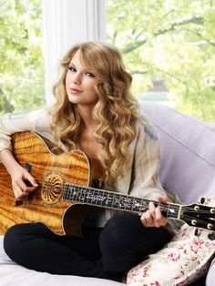 a woman sitting on top of a white couch holding an acoustic guitar in her hands