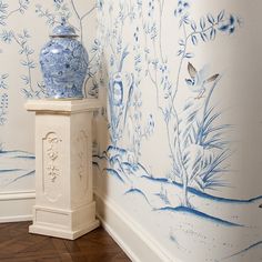 a blue and white vase sitting next to a wall with floral designs on the walls