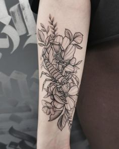 a black and white flower tattoo on the left inner arm, with leaves around it