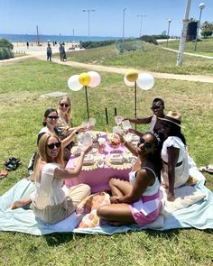 a group of people sitting around a cake on top of a blanket in the grass