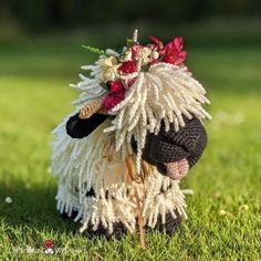 a stuffed sheep with flowers on its head is sitting in the middle of some grass