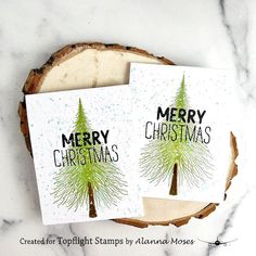 two merry christmas cards sitting on top of a piece of wood next to a slice of tree