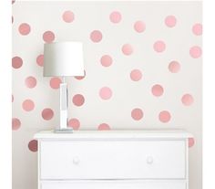 a white dresser with pink polka dot wallpaper and a lamp on top of it