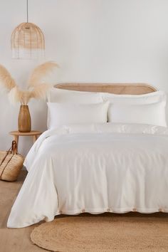 a bed with white sheets and pillows in a room next to a basket on the floor