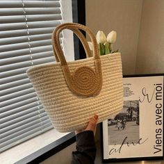 a woman is holding a straw bag with flowers in front of a window and a sign on the wall