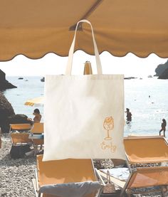 a white bag sitting on top of a beach next to some chairs and umbrellas