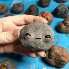 a hand holding a rock with eyes on it and several other rocks in the background