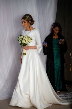 a woman in a white wedding dress holding a bouquet and standing next to another woman