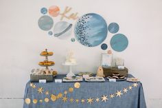 a blue table topped with lots of desserts next to a wall mounted art piece