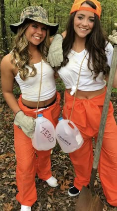 two women dressed in orange pants and white shirts posing for the camera with trees behind them