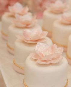 small white cakes with pink flowers on them are sitting on a table in front of other desserts