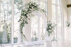 an arch decorated with flowers and greenery in front of large windows at a wedding