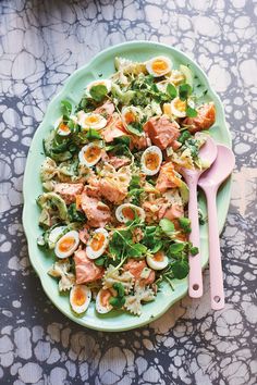 a green plate topped with pasta salad and hard boiled eggs next to pink utensils