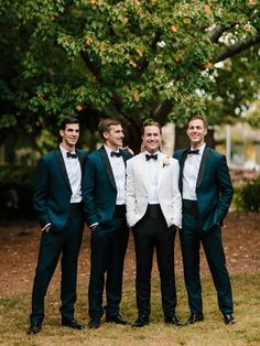 a group of men standing next to each other wearing suits and bow ties in front of a tree