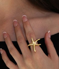 Starfish Ring: ▪️  This gorgeous statement piece will make the perfect gift for yourself or a loved one. The ring is adjustable and will fit different finger sizes   ▪️  Made of gold plated brass   ▪️  The model in the picture is a size 7     Care Instructions:   ▪️  Gold plating can last for years if looked after correctly   ▪️  Keep away from water, sweat, chemicals, perfumes, lotions, etc. If it begins to tarnish in areas of high friction, the color will appear a darker orange   ▪️  How to clean: dip a cotton ball in a solution of mild dish soap and water. Rub gently and then rinse, dry, and buff     We hope you enjoy! We have family ties with jewelers in Istanbul, Turkey who hand make our pieces with love. Your happiness is our utmost priority, and we accept returns if it doesn't meet Gold Rings For Summer Gift, Gold Rings As Summer Gift, Summer Gift Gold Rings, Hellenic Aesthetic, خواتم خطوبة, Starfish Ring, Beach Rings, Fantasy Earrings, Summer Beach Jewelry