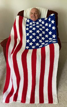 an old man is laying in a chair with a blanket on his head and the american flag draped over him